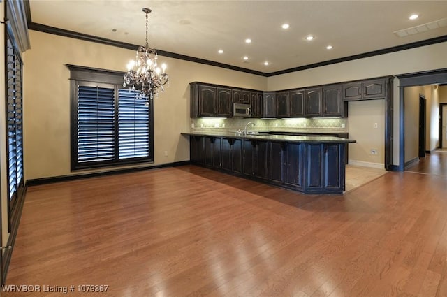 kitchen with a peninsula, wood finished floors, backsplash, stainless steel microwave, and crown molding