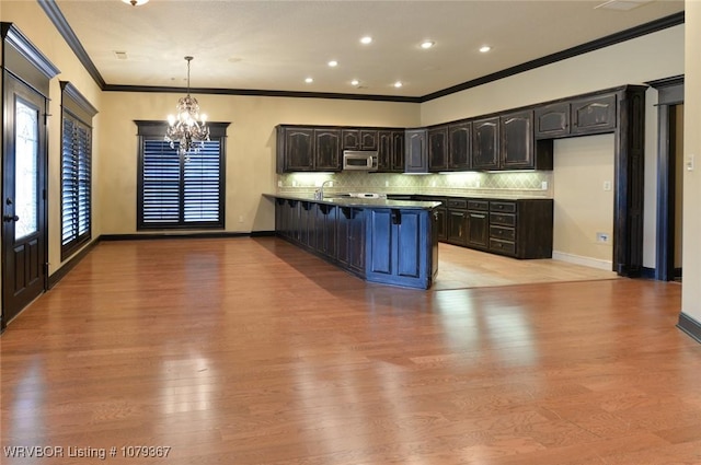 kitchen featuring a notable chandelier, stainless steel microwave, decorative backsplash, light wood-style floors, and a peninsula