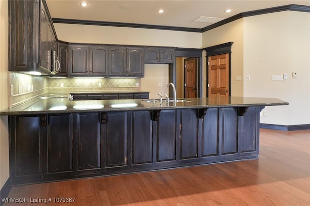 kitchen featuring dark wood-style floors, backsplash, a sink, and a peninsula