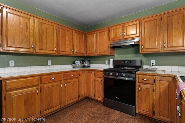 451 Hill St, Booneville, AR 72927 - kitchen with under cabinet range hood, gas stove, tile countertops, dark wood-type flooring, and brown cabinetry