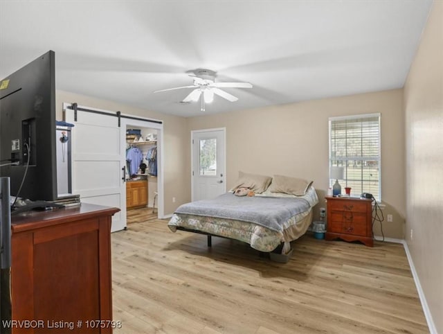 bedroom featuring ceiling fan, a barn door, light wood-type flooring, and multiple windows