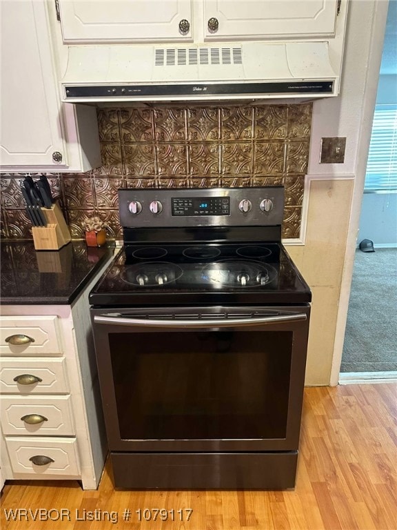 kitchen featuring electric stove, light wood finished floors, exhaust hood, and white cabinetry