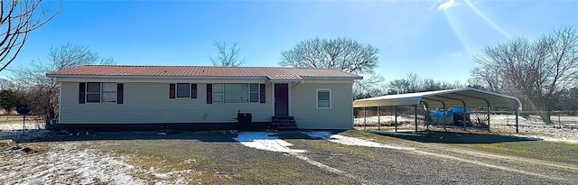 manufactured / mobile home with driveway, entry steps, metal roof, fence, and a carport