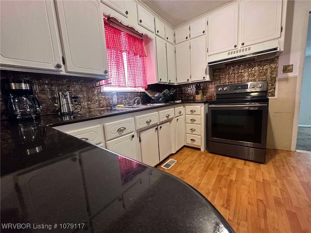 kitchen with under cabinet range hood, a sink, white cabinets, stainless steel electric stove, and dark countertops