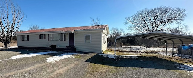 view of front of home featuring dirt driveway, a detached carport, entry steps, metal roof, and fence