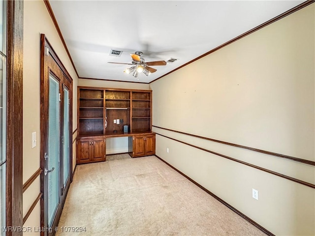 unfurnished office featuring built in desk, visible vents, light colored carpet, ornamental molding, and a ceiling fan