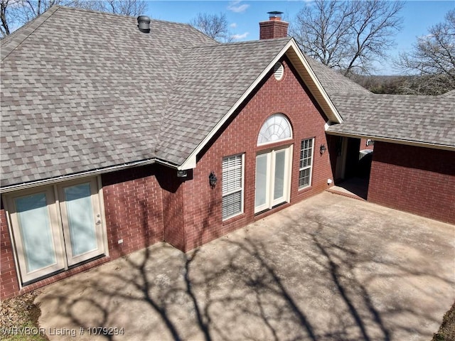 view of side of home with brick siding, a chimney, and roof with shingles