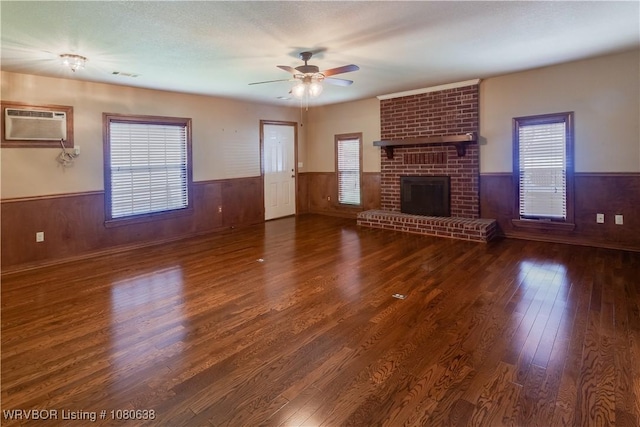 unfurnished living room with a ceiling fan, a wall unit AC, wood finished floors, and a wainscoted wall