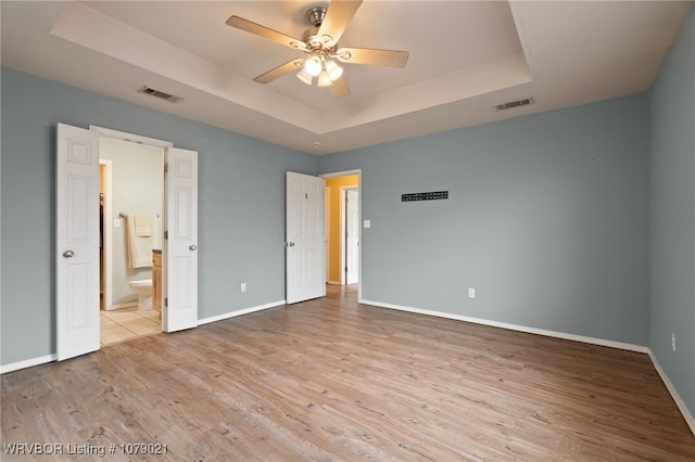 unfurnished bedroom with a raised ceiling, connected bathroom, ceiling fan, and light hardwood / wood-style flooring