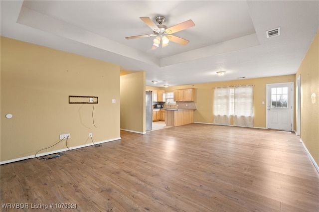 unfurnished living room with a raised ceiling, sink, ceiling fan, and light hardwood / wood-style flooring