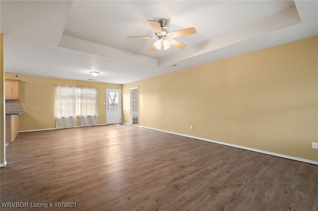 empty room with dark hardwood / wood-style floors, ceiling fan, and a tray ceiling