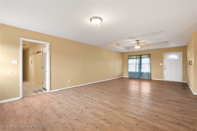 unfurnished living room with a raised ceiling, ceiling fan, and light hardwood / wood-style floors