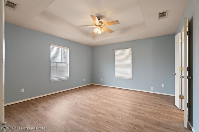 empty room with a raised ceiling, ceiling fan, and light wood-type flooring