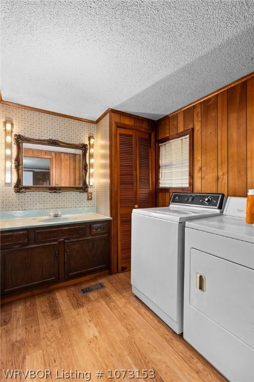 washroom featuring washing machine and clothes dryer, sink, cabinets, ornamental molding, and light wood-type flooring