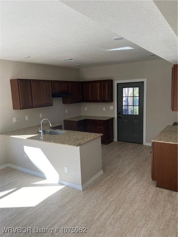 kitchen with kitchen peninsula, a textured ceiling, light wood-type flooring, and sink