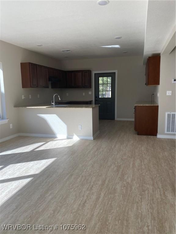 kitchen with kitchen peninsula, dark brown cabinetry, sink, and light hardwood / wood-style floors