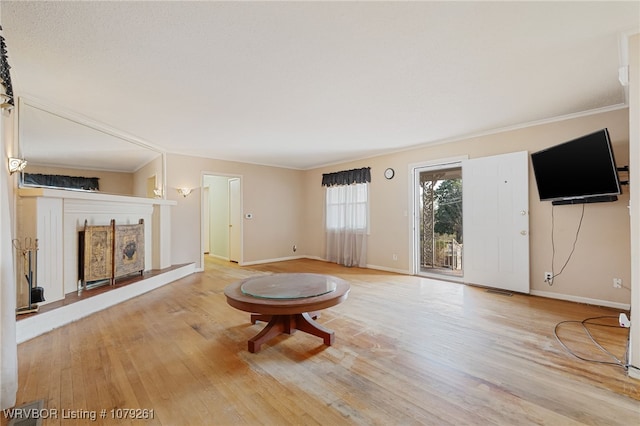 unfurnished living room featuring a fireplace with raised hearth, crown molding, baseboards, and wood finished floors