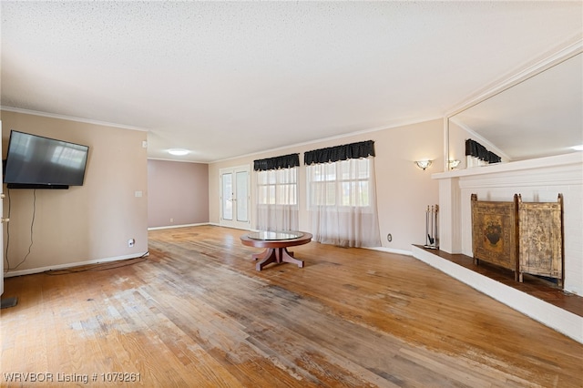 unfurnished living room featuring a textured ceiling, ornamental molding, wood-type flooring, and baseboards