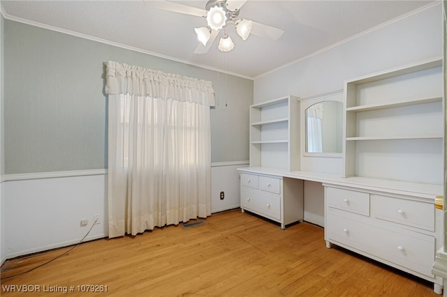 unfurnished bedroom with built in desk, light wood finished floors, visible vents, ornamental molding, and a ceiling fan