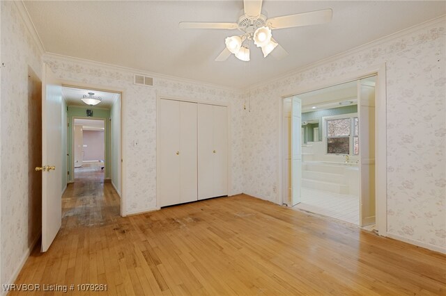 unfurnished bedroom featuring crown molding, light wood finished floors, visible vents, baseboards, and wallpapered walls