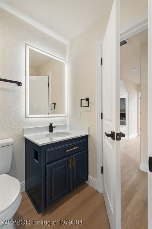 half bathroom featuring baseboards, vanity, toilet, and wood finished floors