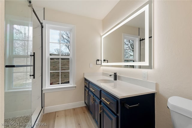 bathroom with toilet, vanity, wood finished floors, baseboards, and walk in shower