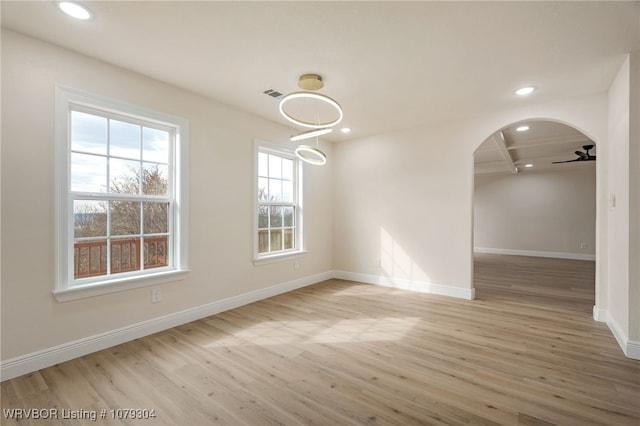 empty room featuring arched walkways, recessed lighting, baseboards, and wood finished floors