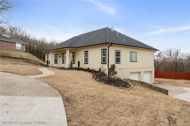 view of front facade featuring driveway, a shingled roof, an attached garage, and fence