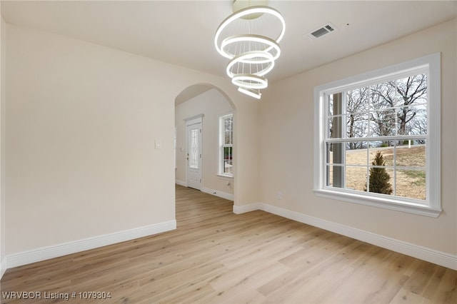 unfurnished dining area with arched walkways, visible vents, a notable chandelier, and baseboards