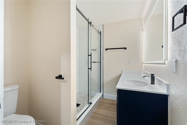 bathroom with toilet, wood finished floors, a shower stall, and vanity