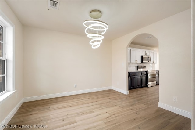 unfurnished dining area featuring arched walkways, visible vents, a chandelier, light wood-type flooring, and baseboards