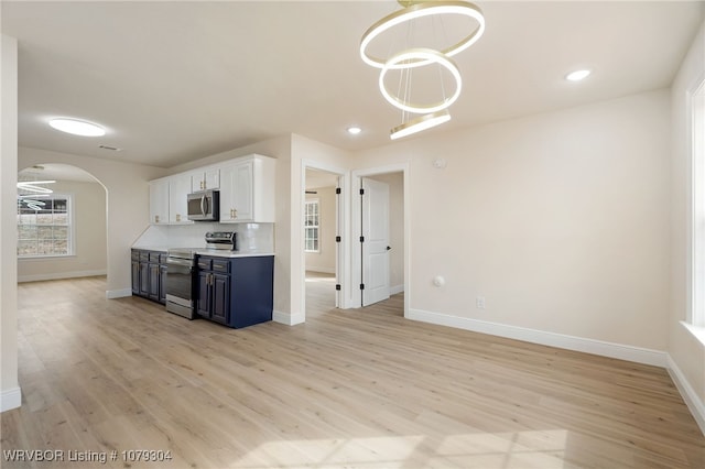 kitchen with appliances with stainless steel finishes, arched walkways, white cabinetry, and light wood-style flooring