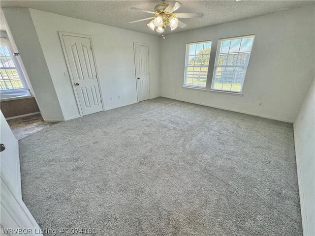 unfurnished bedroom featuring a textured ceiling, light colored carpet, ceiling fan, and multiple closets