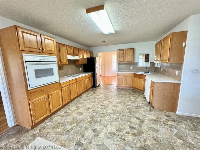 kitchen featuring a textured ceiling, white appliances, tasteful backsplash, and sink