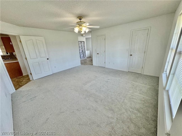 unfurnished bedroom with light carpet, a textured ceiling, ceiling fan, and multiple closets