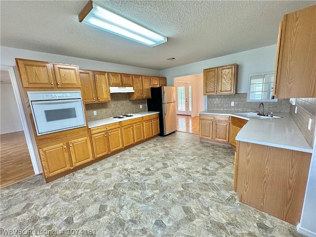 kitchen with a textured ceiling, decorative backsplash, white appliances, and sink