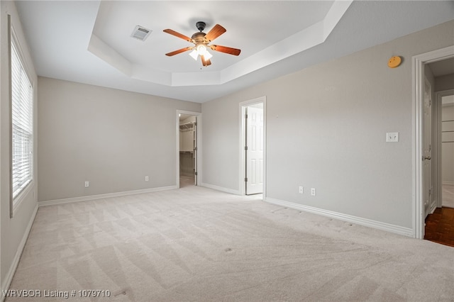 unfurnished bedroom featuring a spacious closet, light colored carpet, baseboards, visible vents, and a raised ceiling