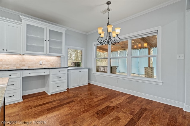 unfurnished dining area featuring built in desk, visible vents, baseboards, an inviting chandelier, and dark wood finished floors