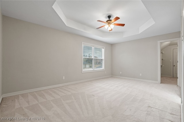 unfurnished bedroom featuring a ceiling fan, light carpet, a raised ceiling, and baseboards