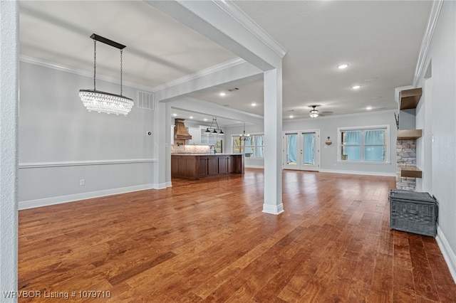 unfurnished living room featuring wood finished floors, ceiling fan with notable chandelier, baseboards, visible vents, and crown molding