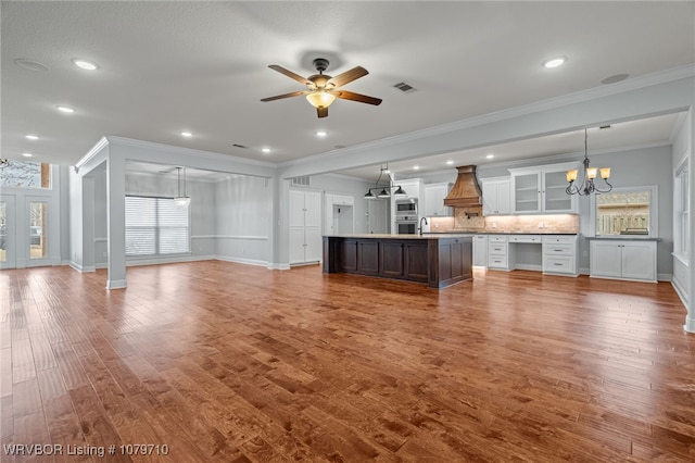 unfurnished living room featuring dark wood-style floors, a sink, crown molding, visible vents, and ceiling fan with notable chandelier