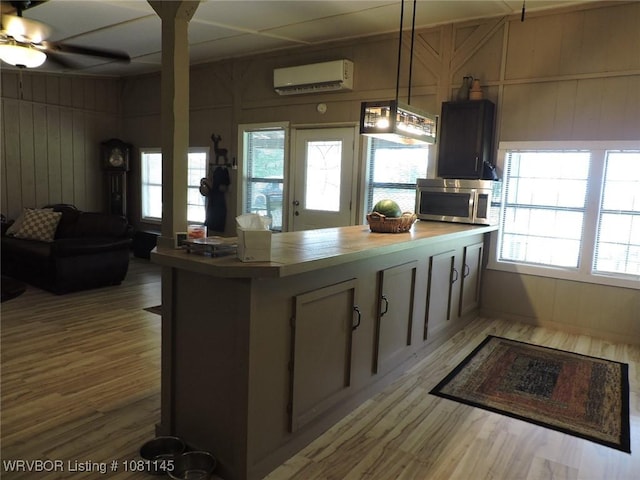 19108 Canova Trl, Mountainburg, AR 72946 - kitchen with a wall unit AC, light wood-style flooring, stainless steel microwave, a peninsula, and wood walls