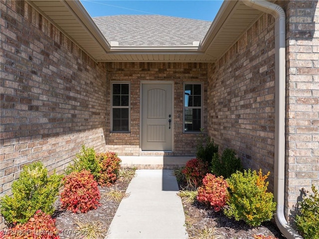 entrance to property featuring brick siding and a shingled roof