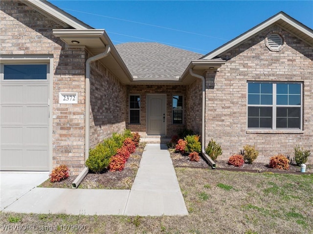 doorway to property with an attached garage, brick siding, and a shingled roof