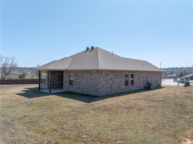 view of property exterior featuring a patio, roof with shingles, a yard, central AC, and brick siding