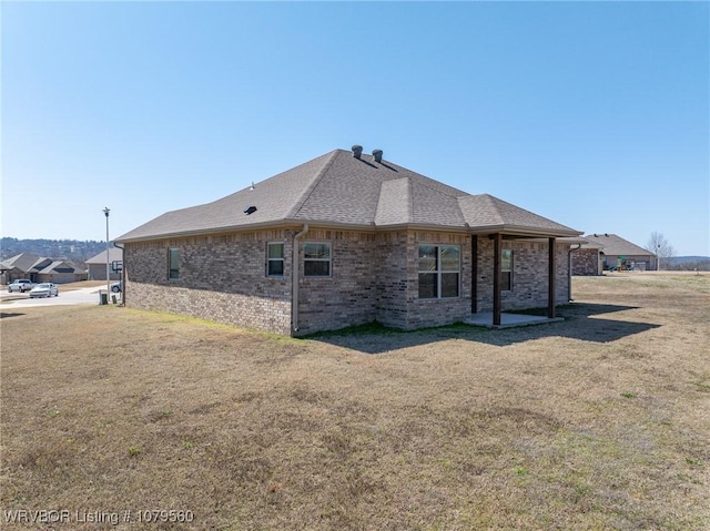 back of property with brick siding, a lawn, and roof with shingles