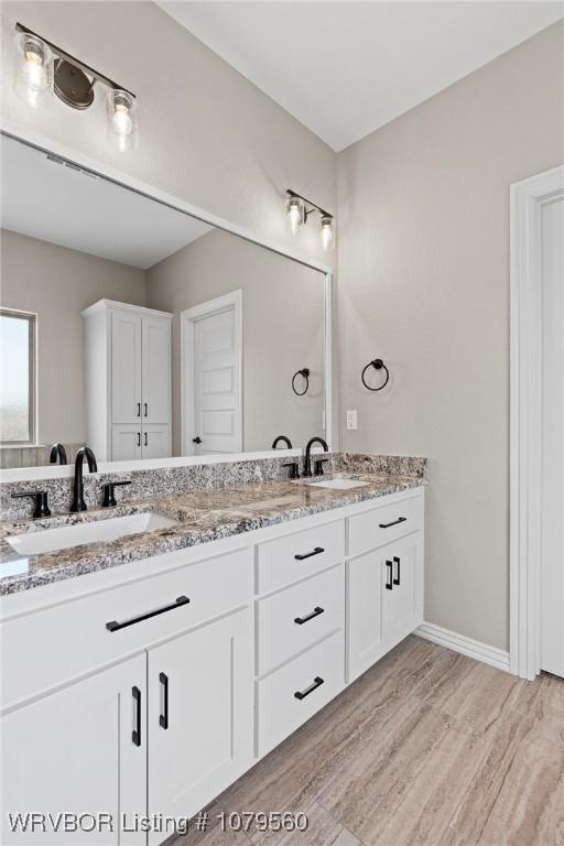 bathroom with double vanity, wood finished floors, baseboards, and a sink