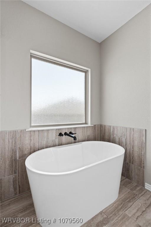 bathroom featuring tile walls, a wealth of natural light, and a freestanding bath