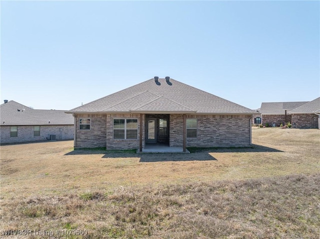 rear view of property with a patio area, a lawn, a shingled roof, and brick siding