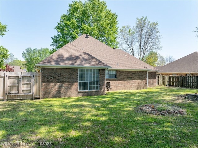 back of property with brick siding, a lawn, a fenced backyard, and a gate